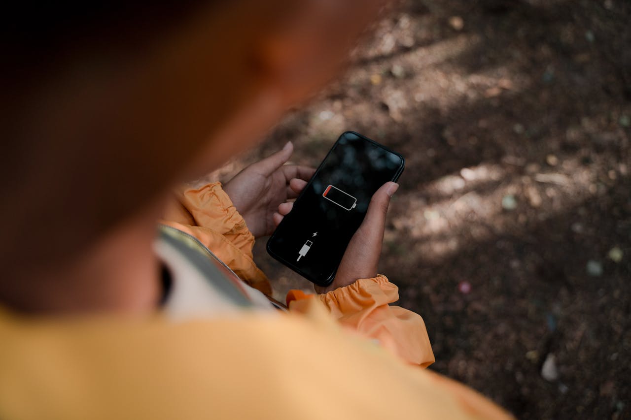 Um adolescente segura um smartphone exibindo bateria fraca ao ar livre em uma floresta.