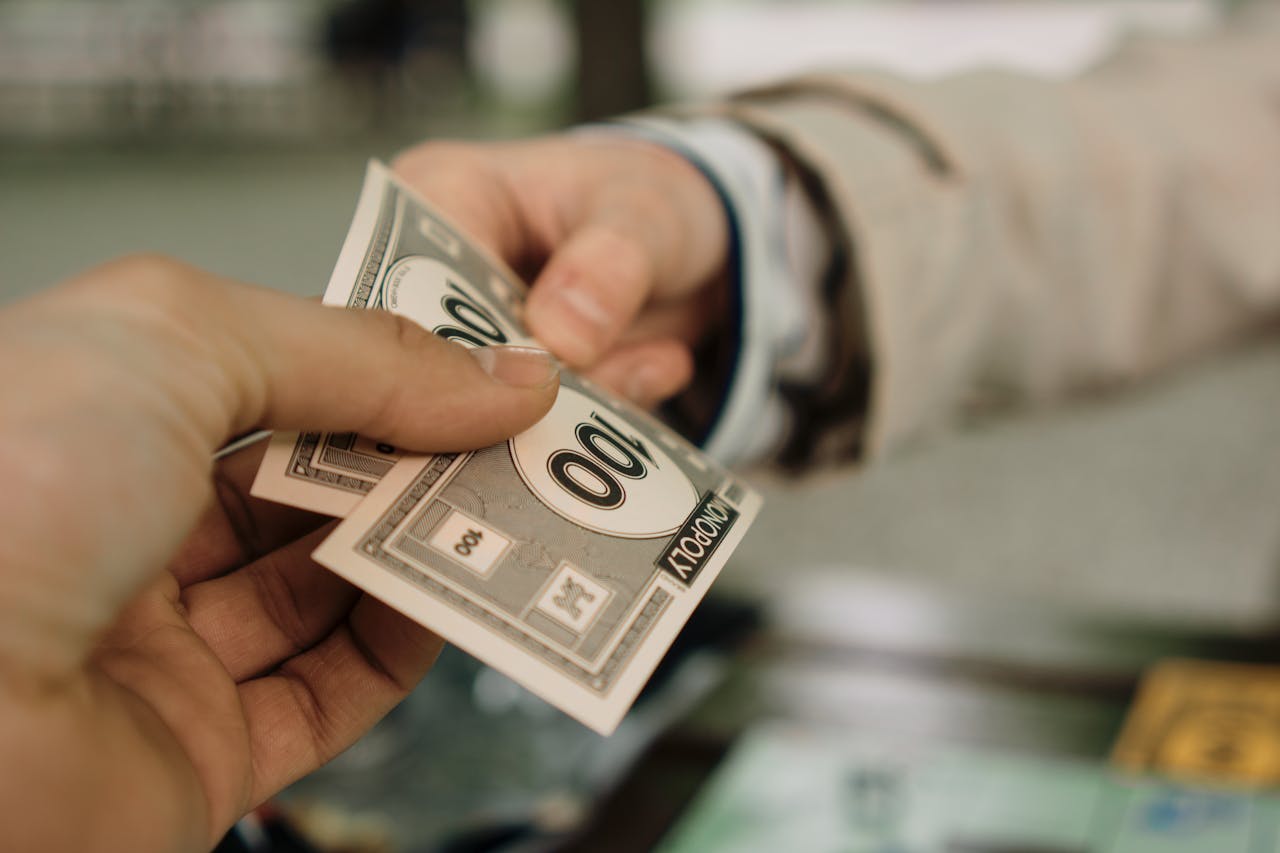 Close-up de duas mãos trocando dinheiro de Banco Imobiliário, simbolizando uma transação financeira.