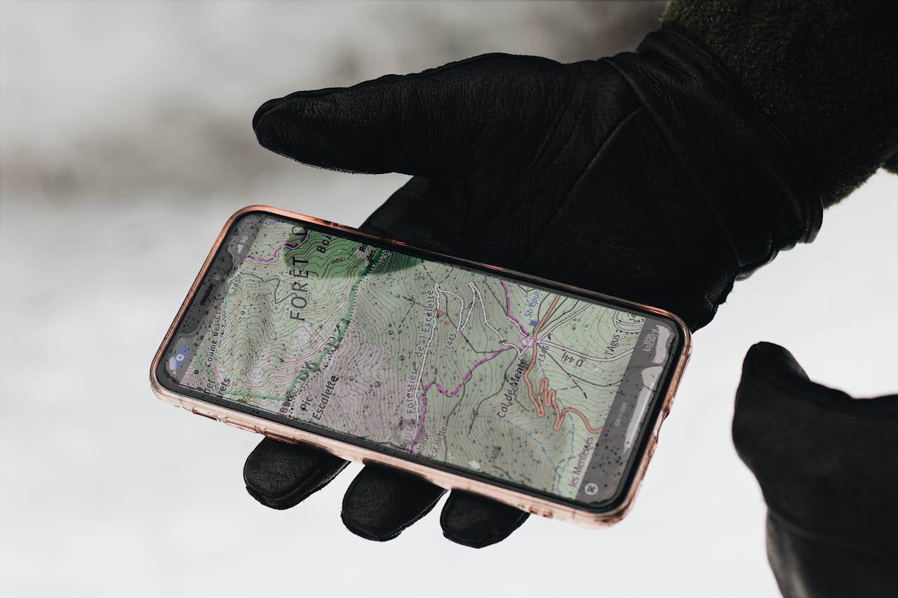 Uma mão enluvada segura um smartphone com um aplicativo de mapa exibido, mostrando navegação em clima frio.