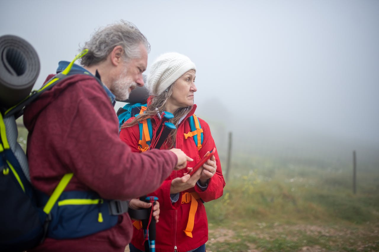 Dois caminhantes consultam um smartphone em uma paisagem rural nevoenta em Portugal.
