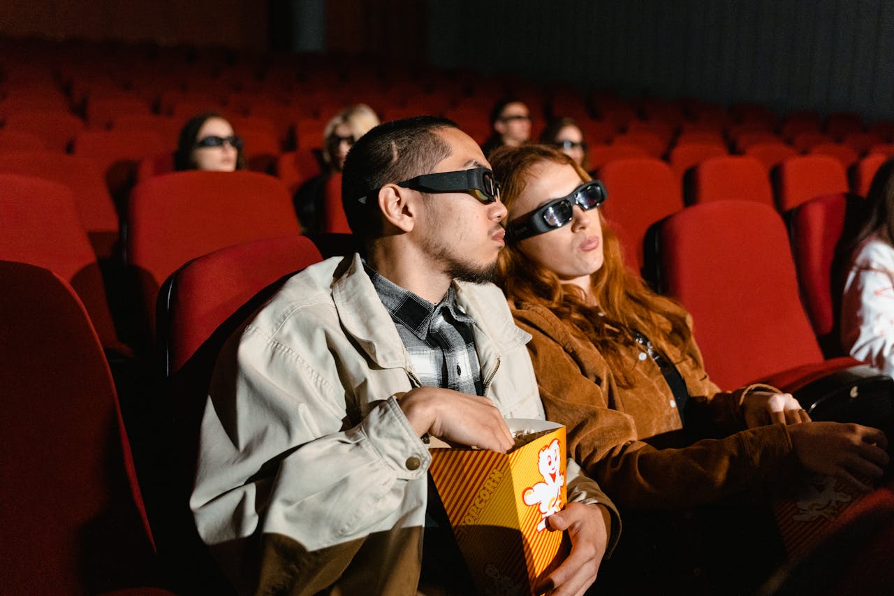 Casal usando óculos 3D assistindo a um filme em um cinema, comendo pipoca.
