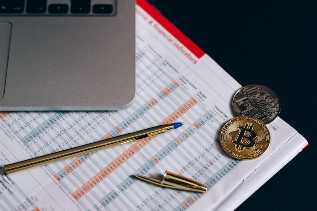 Folha com caneta, notebook e bitcoin por cima.